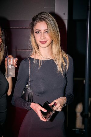Nightclub attendee in dark outfit holding drinks during evening event.