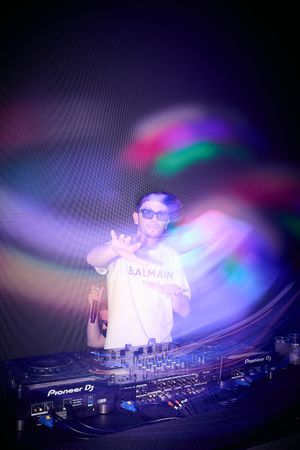 DJ performing behind decks with colorful light effects creating atmospheric ambiance.