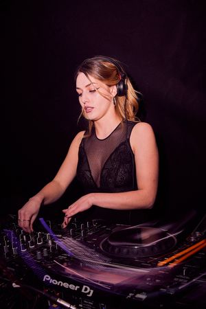 Female DJ mixing music on Pioneer equipment in dark nightclub setting.