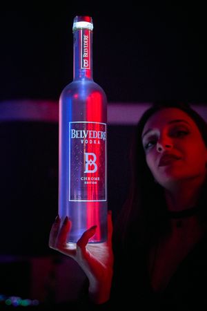 Illuminated Belvedere vodka bottle glowing with red and blue lighting in a dark nightclub setting.
