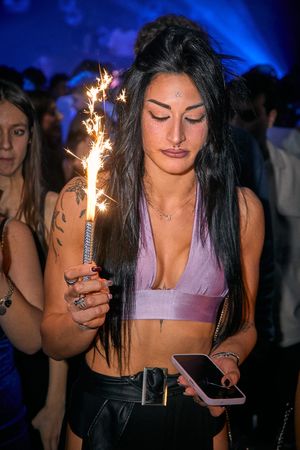 Partygoer holding a sparkler in a crowded nightclub with blue lighting.