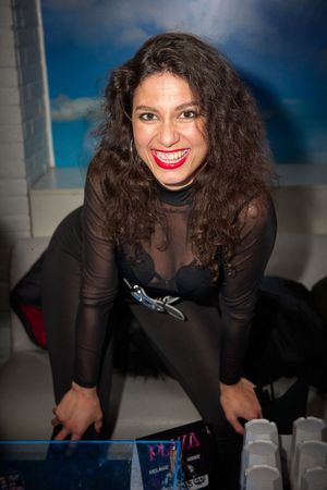 Person in black sheer outfit smiling while leaning over at a party.