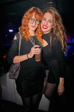 Two friends enjoying drinks and posing together at a nightclub.