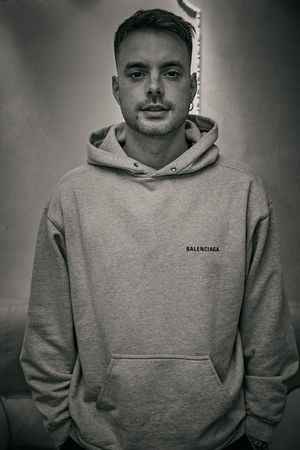 Monochrome portrait of person wearing gray Balenciaga hoodie against plain background.