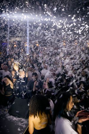 Nightclub crowd celebrating under falling confetti and bright spotlights.