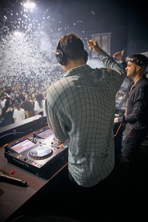 DJ performing at turntables while confetti rains down at packed nightclub.