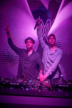 Two DJs performing on stage with purple lighting and Pioneer equipment.