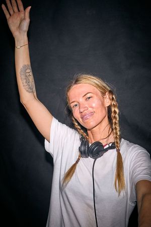 DJ with braided hair and headphones raising hand during performance.
