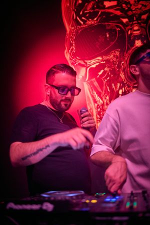 DJs performing in nightclub under red lighting with decorative skull backdrop.