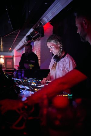 DJ performing at mixing console under red and ambient lighting.