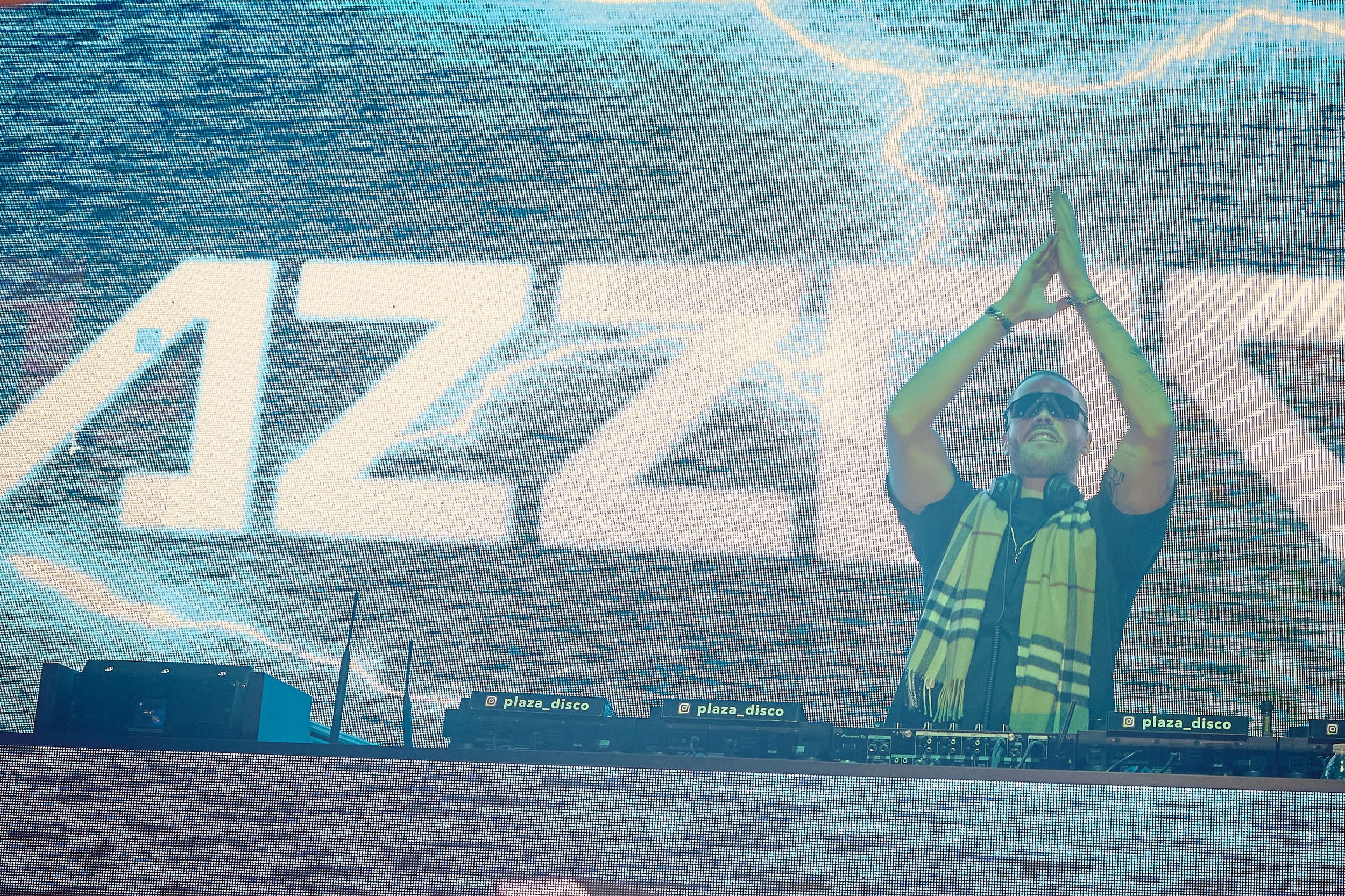 Concert stage with performer silhouetted against blue digital display and lightning effect.