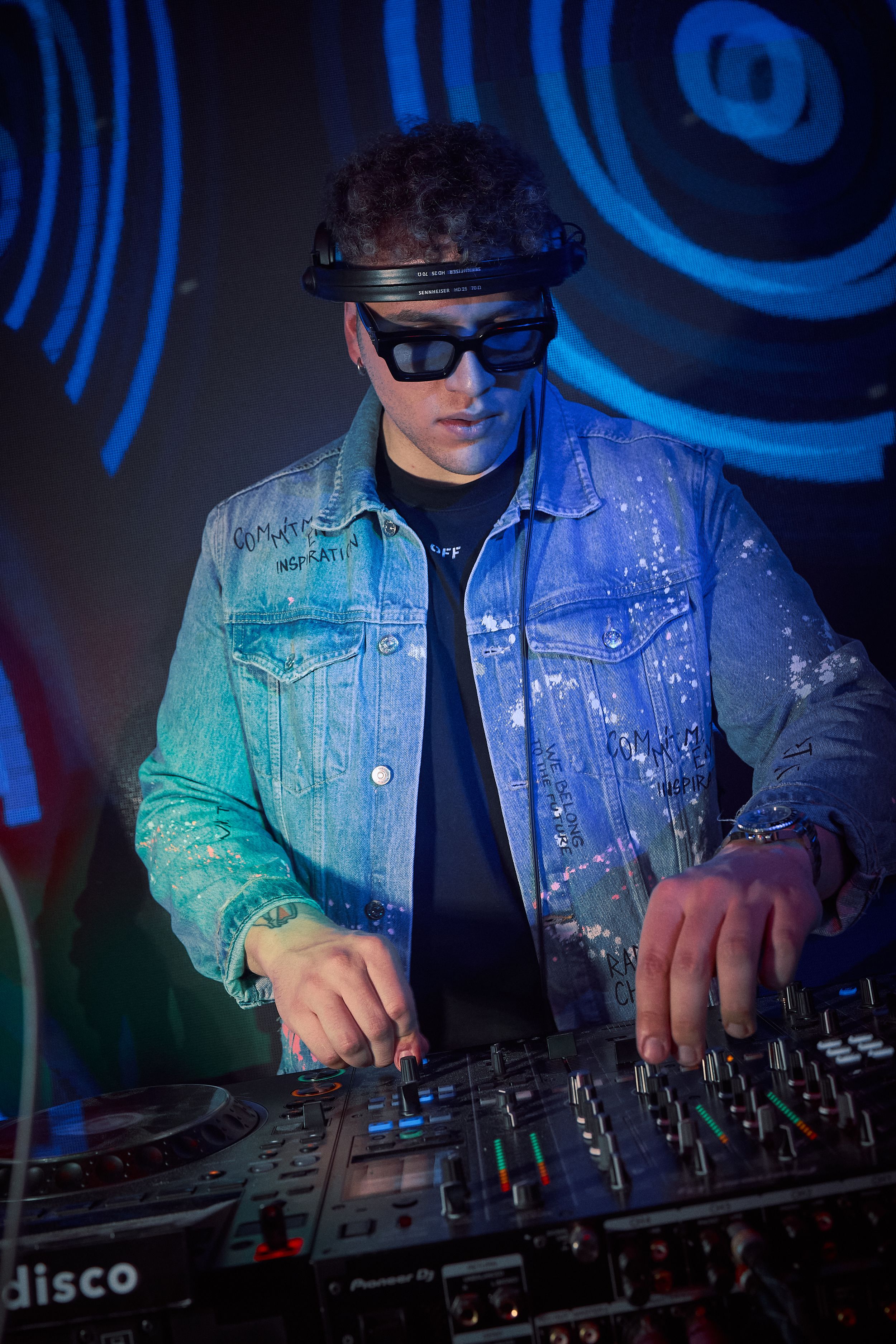 DJ mixing music on turntables in a nightclub with blue lighting and denim jacket.