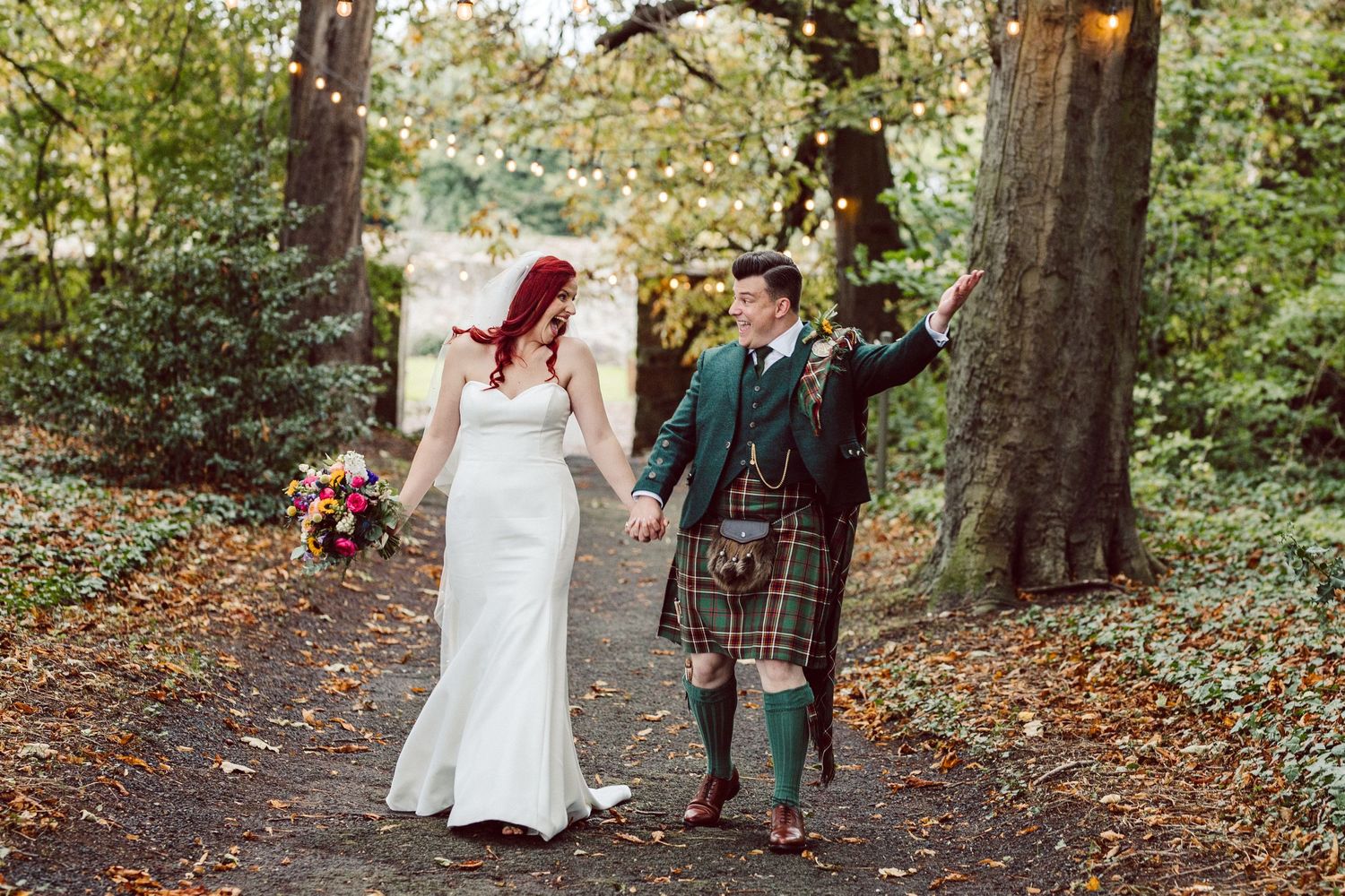 Couple strolling through autumn woods with string lights creating romantic ambiance.