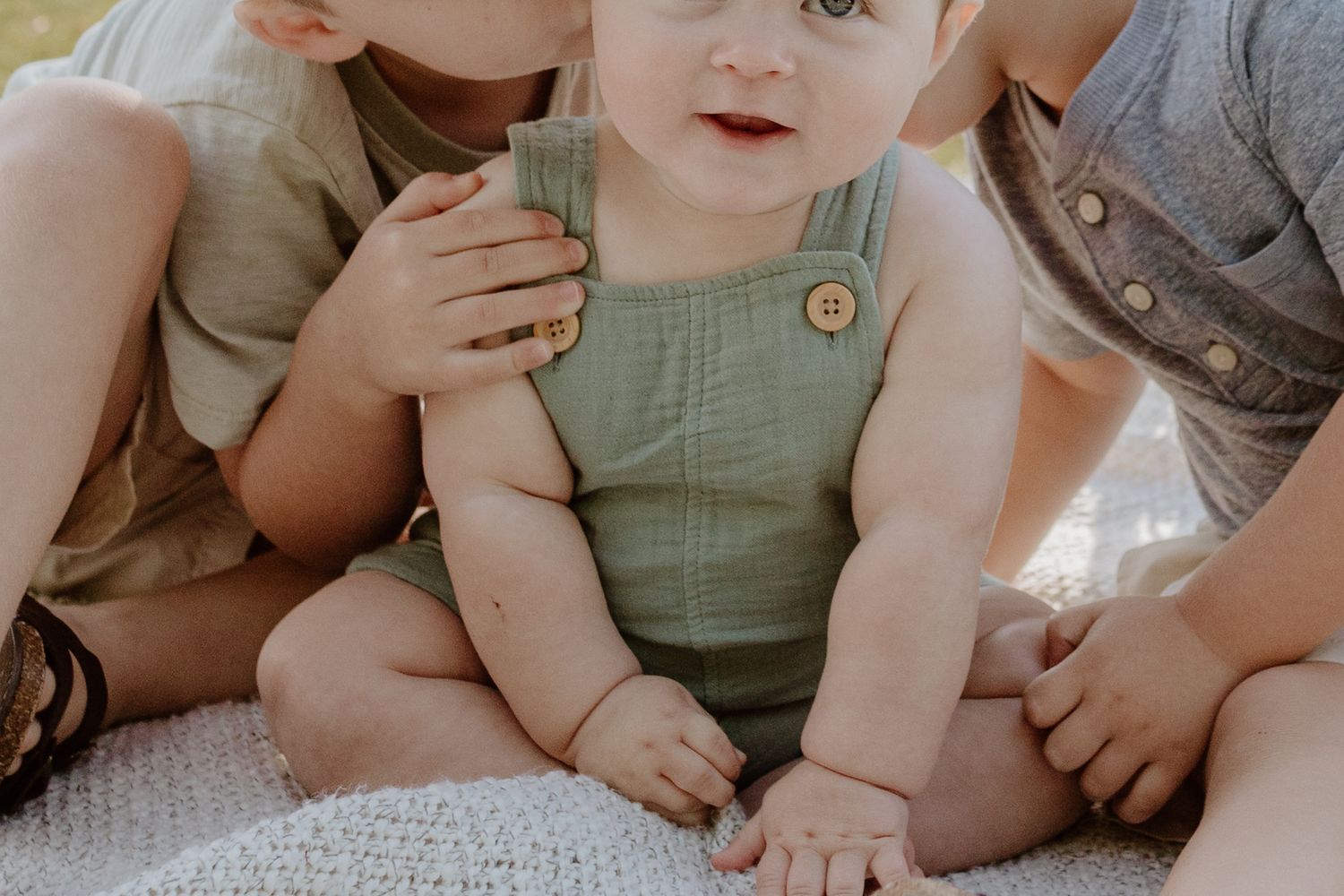 Close up of baby in green overalls sitting on blanket during outdoor session.