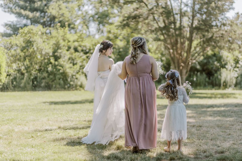 Wedding party in pastel dresses gathered outdoors on sunny day with trees in background.
