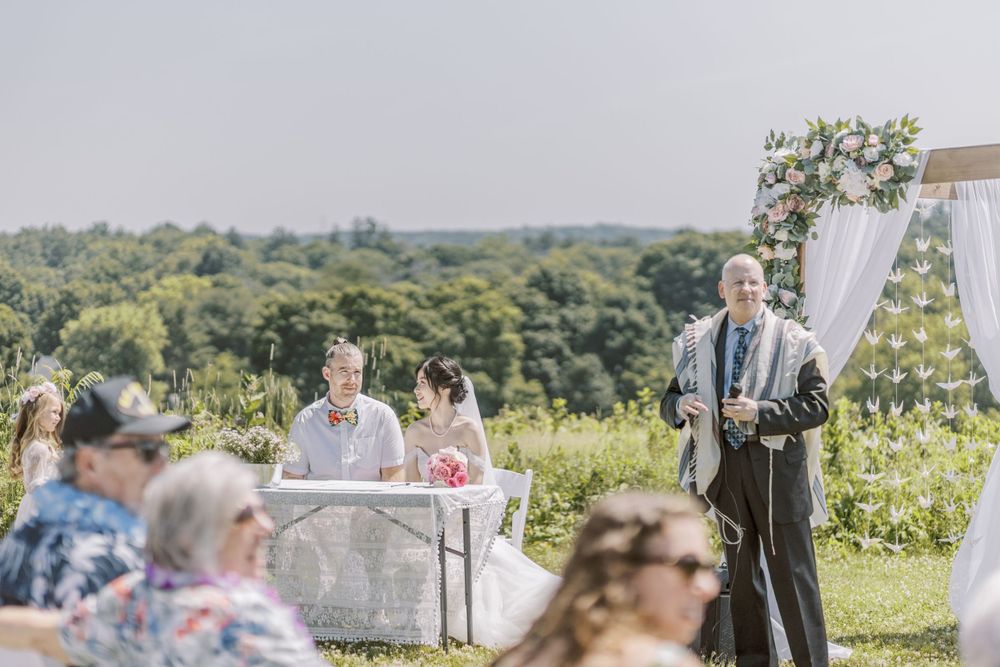 Wedding ceremony overlooking scenic hillside with white decor and floral arrangements.