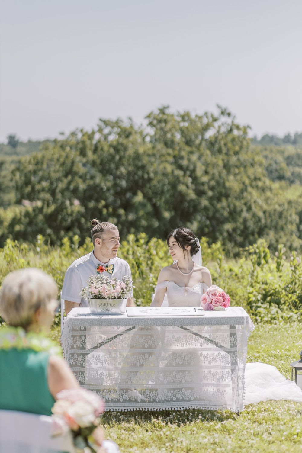 Couple seated on decorative white settee during outdoor hilltop wedding ceremony.