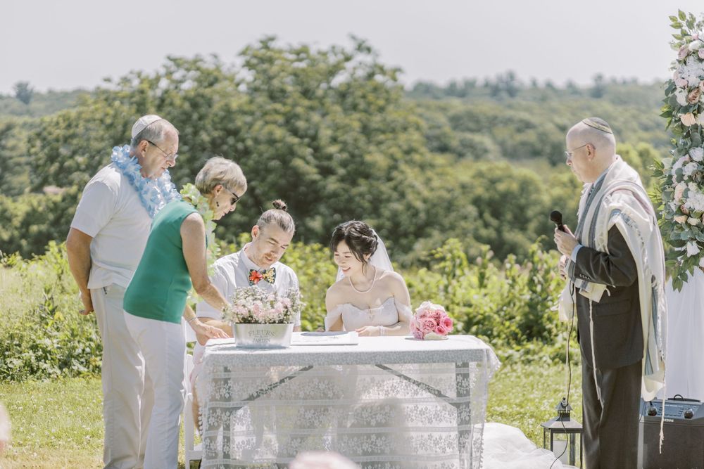 Elegant outdoor wedding ceremony setup with white draped arches and floral decorations in a scenic hilltop location.