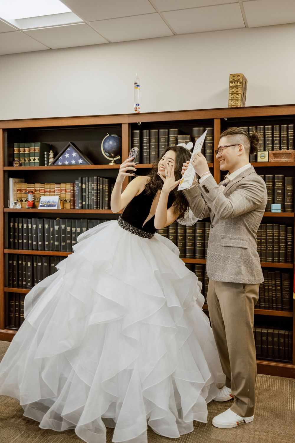 Playful couple poses dramatically in library with bookshelves.
