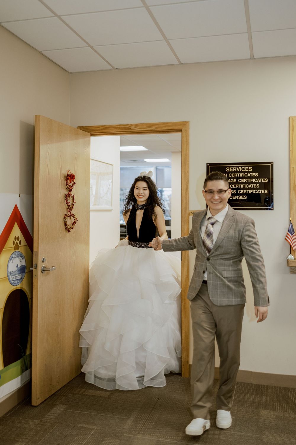 Couple poses playfully by office door with American flag visible.
