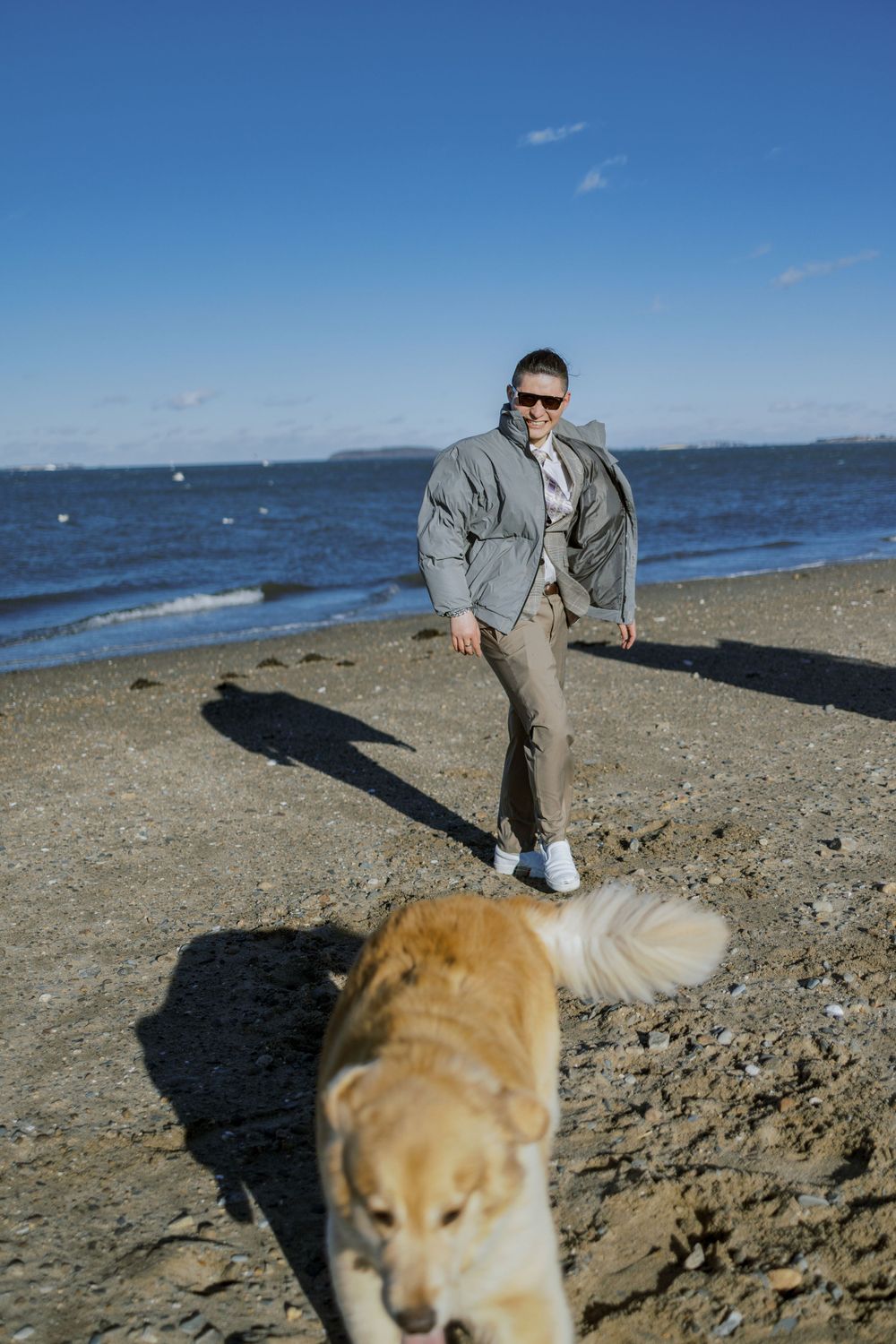 A golden retriever joins a beach photoshoot with someone wearing a gray suit.