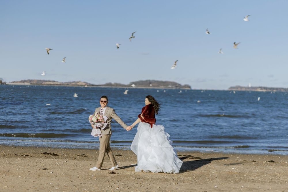 A couple shares a romantic moment on a sandy beach with seagulls and ocean views.