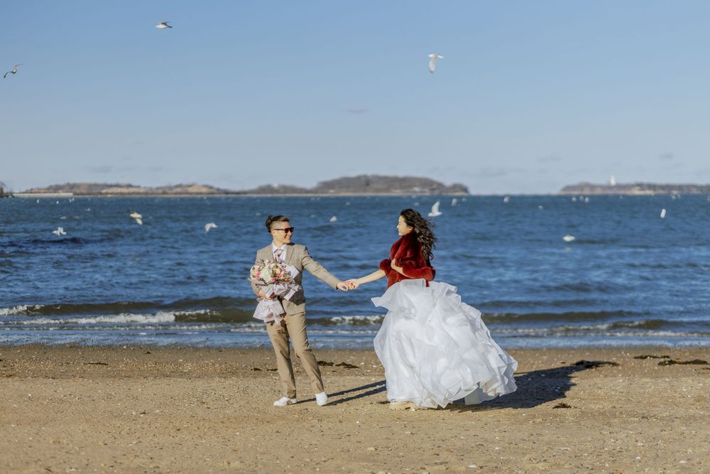 A couple dances on the beach during their wedding photoshoot with seagulls in flight.