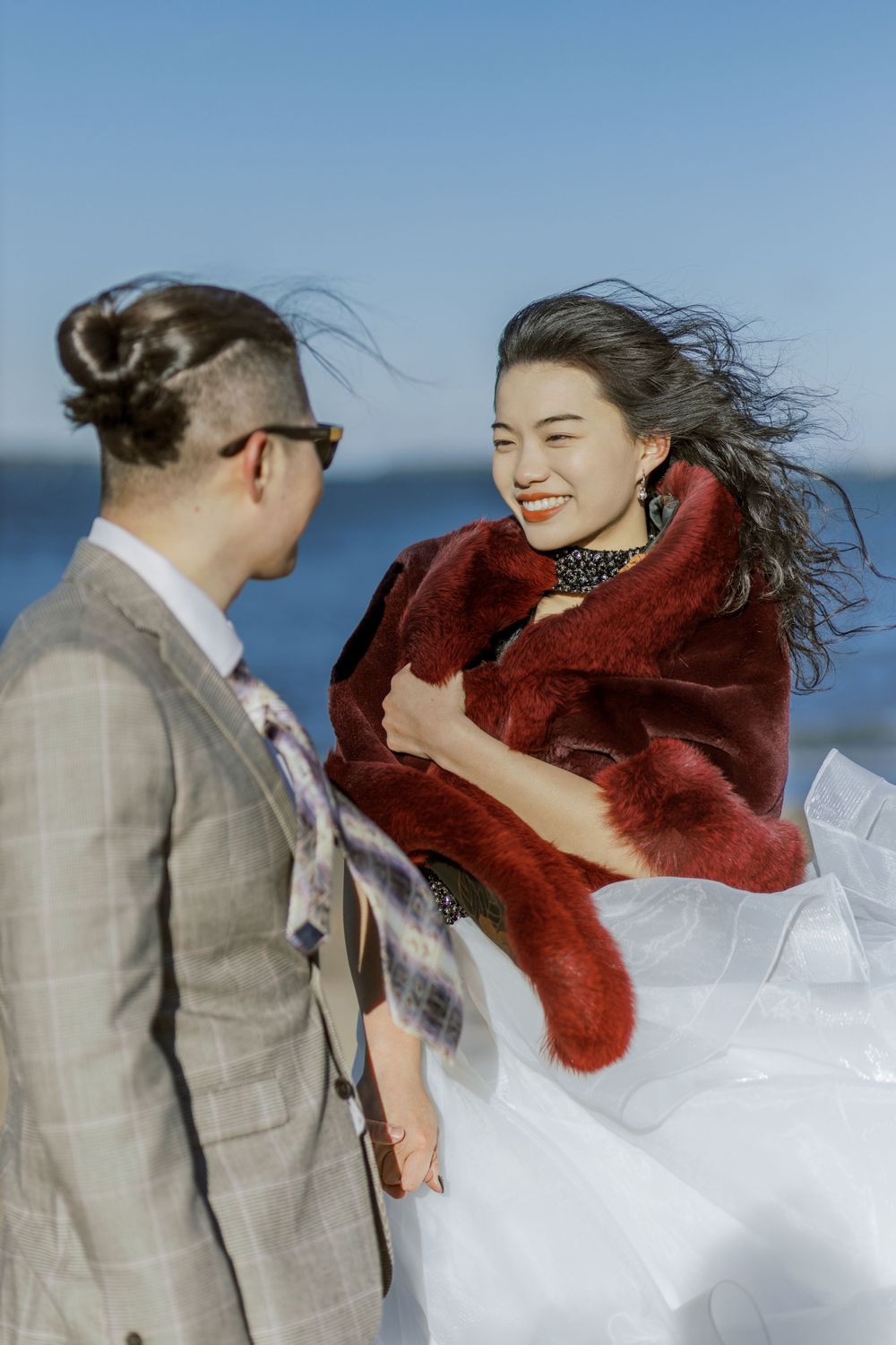 A couple shares a joyful moment in formal wear with the ocean breeze blowing.