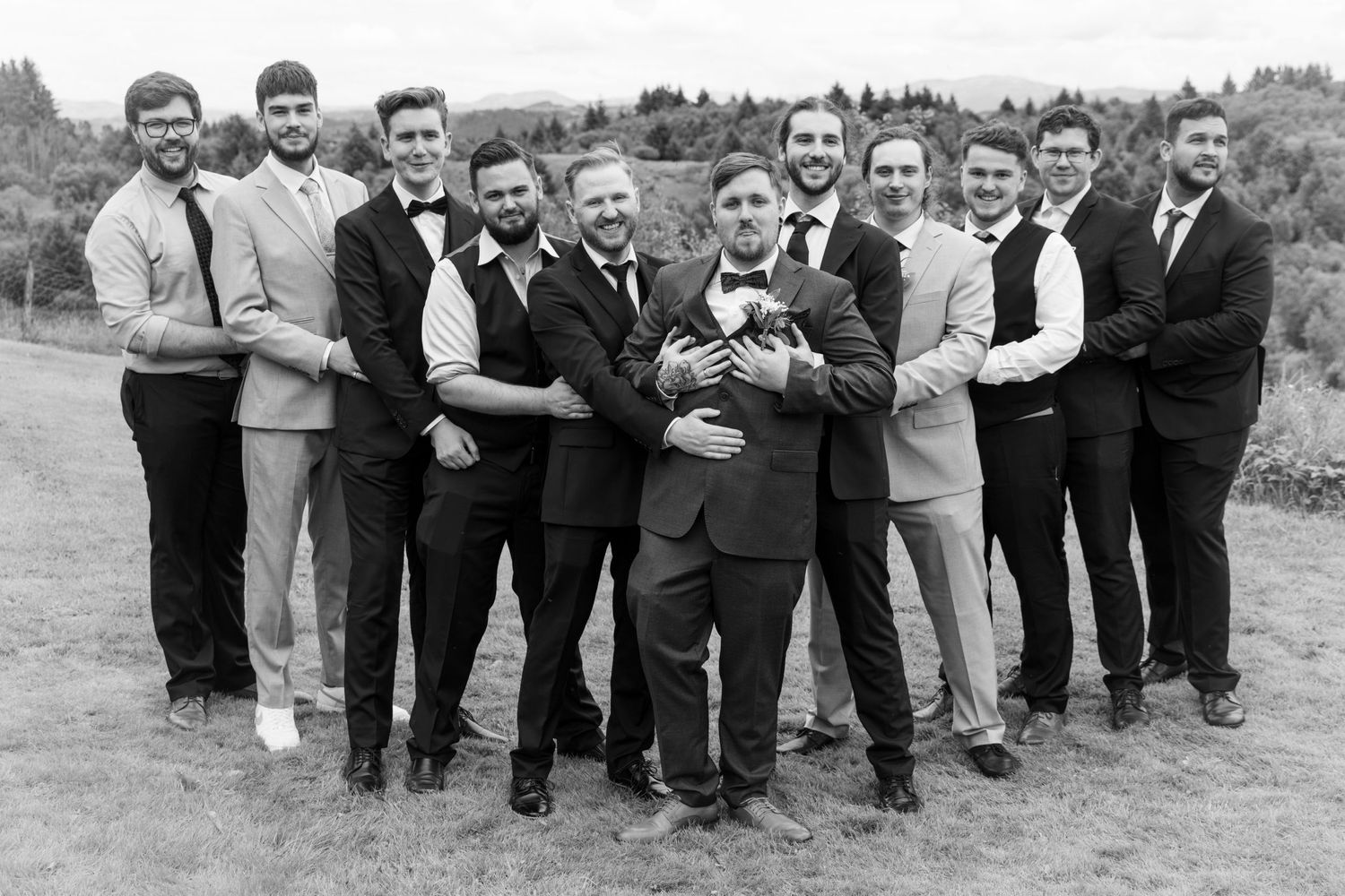 Black and white photo of groom and groomsmen posing together outdoors at a wedding.