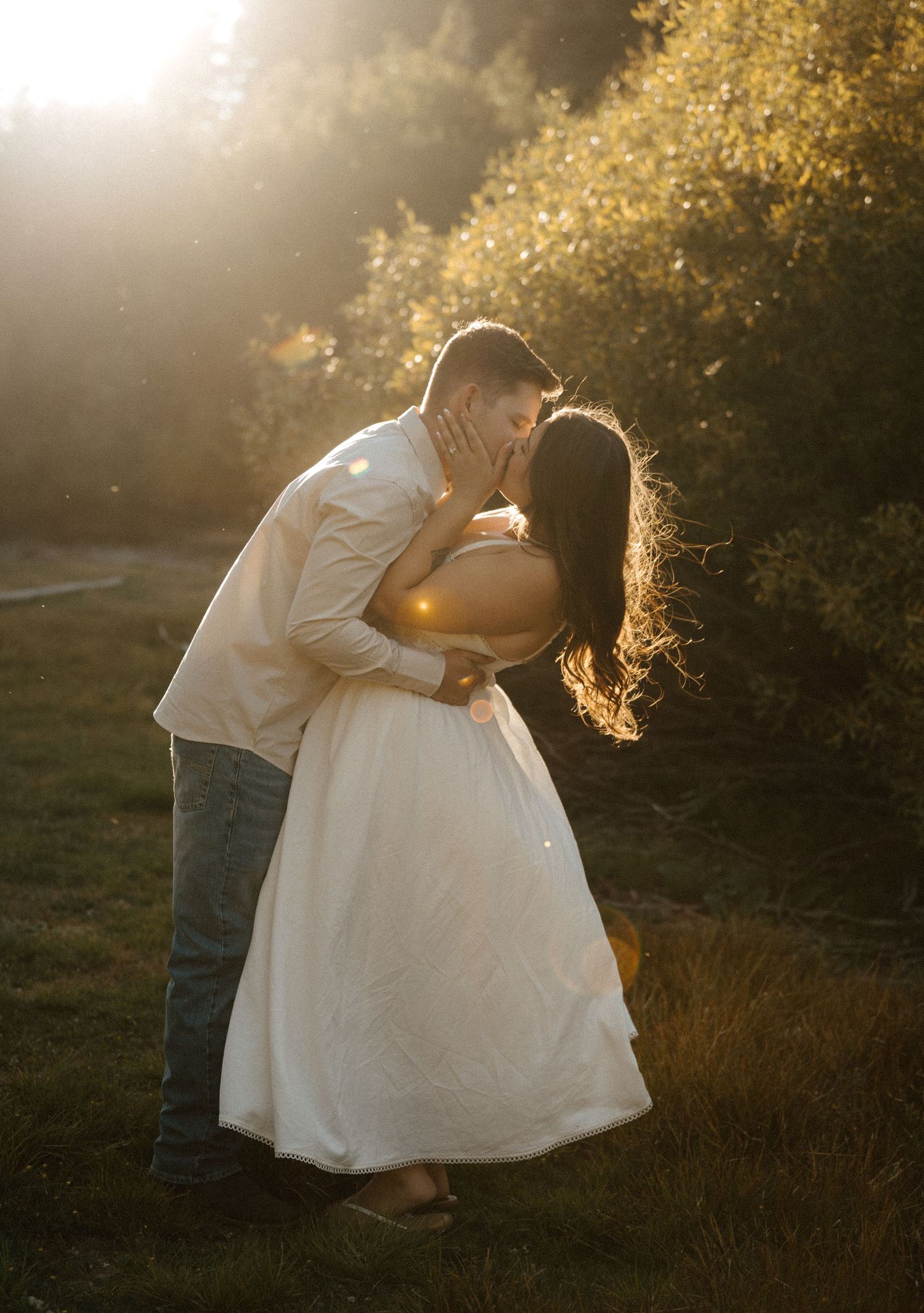 Couple sharing a romantic kiss on a rocky beach at golden hour sunset.