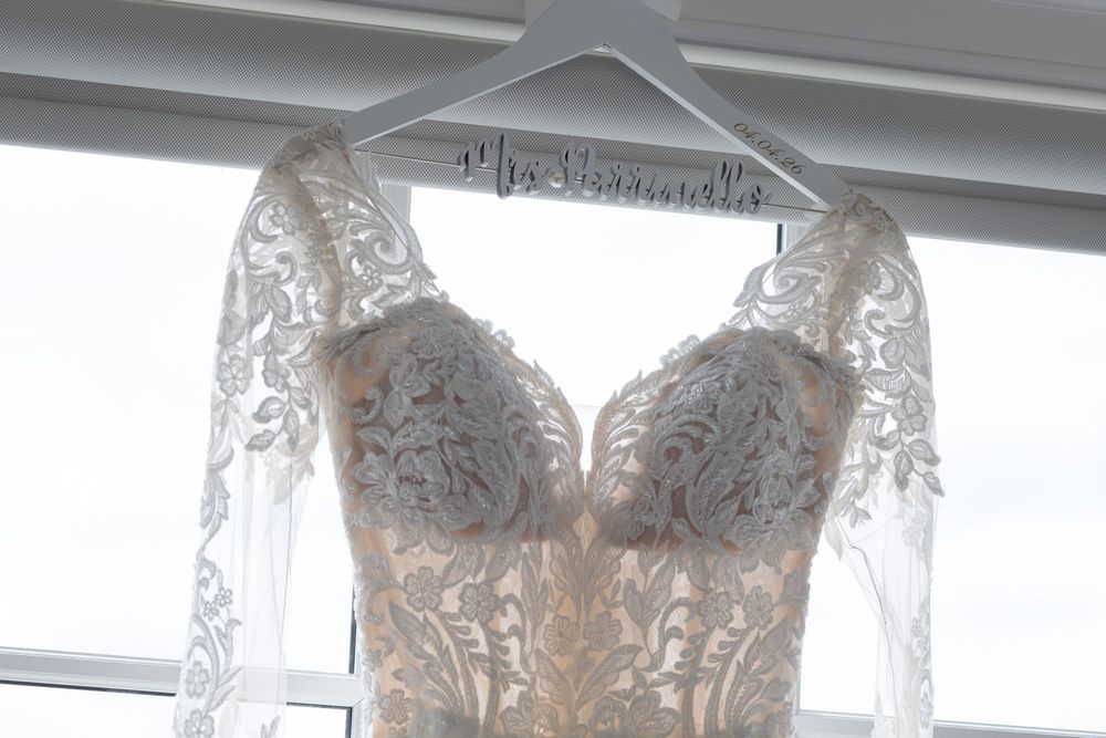 Elegant lace wedding dress hanging on a personalized Mrs. Hainneville hanger against a bright window.