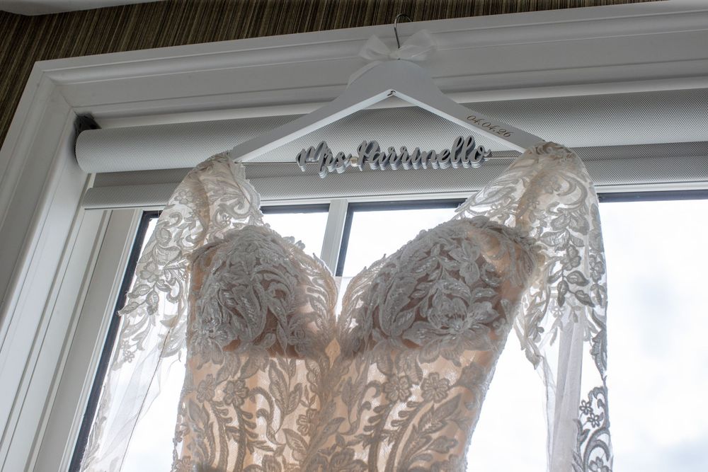 Lace wedding dress on a custom personalized bridal hanger displayed in a bright window.