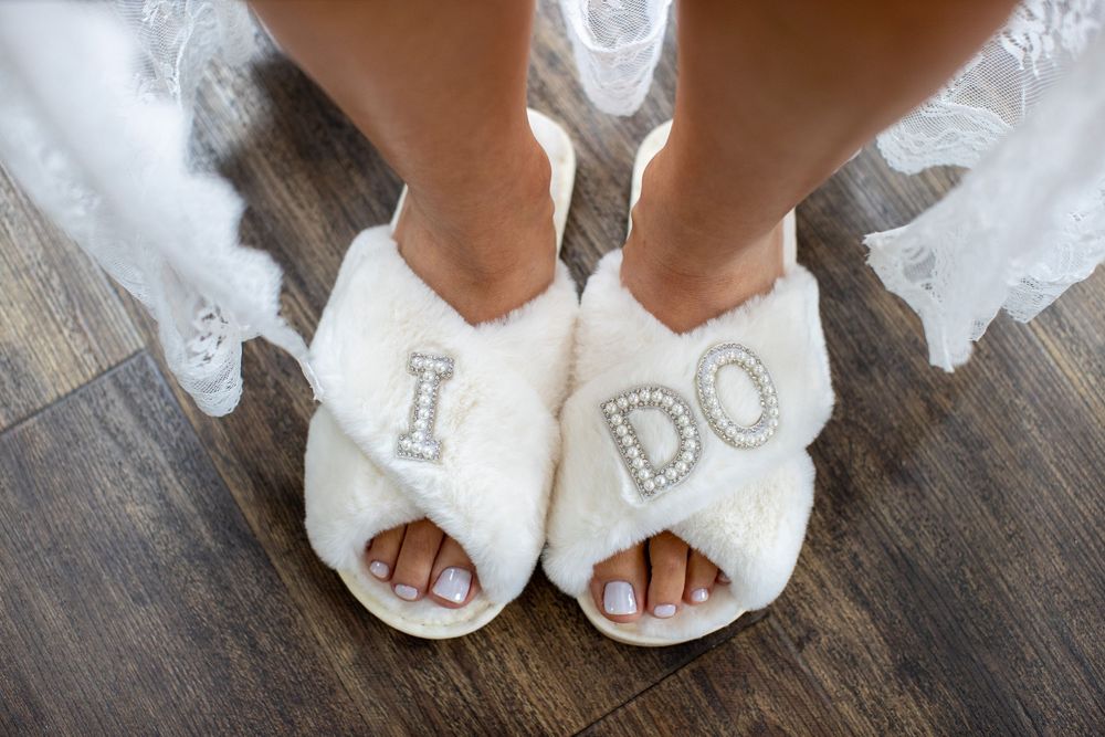 Bride wearing white fluffy I DO rhinestone slippers on wedding day.
