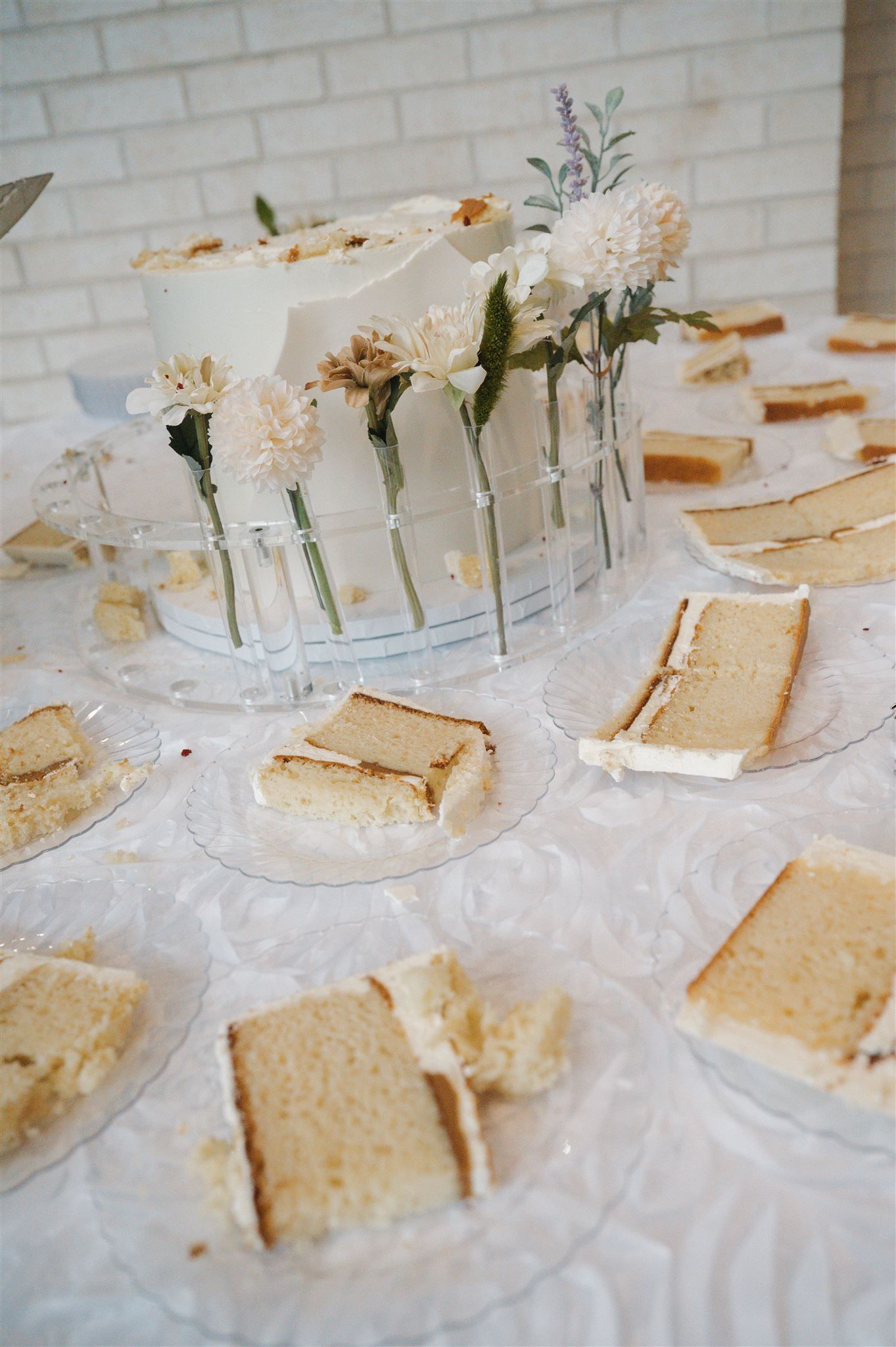 White carnations in bud vases displayed alongside tea sandwiches on a white tablecloth at an elegant party setting.