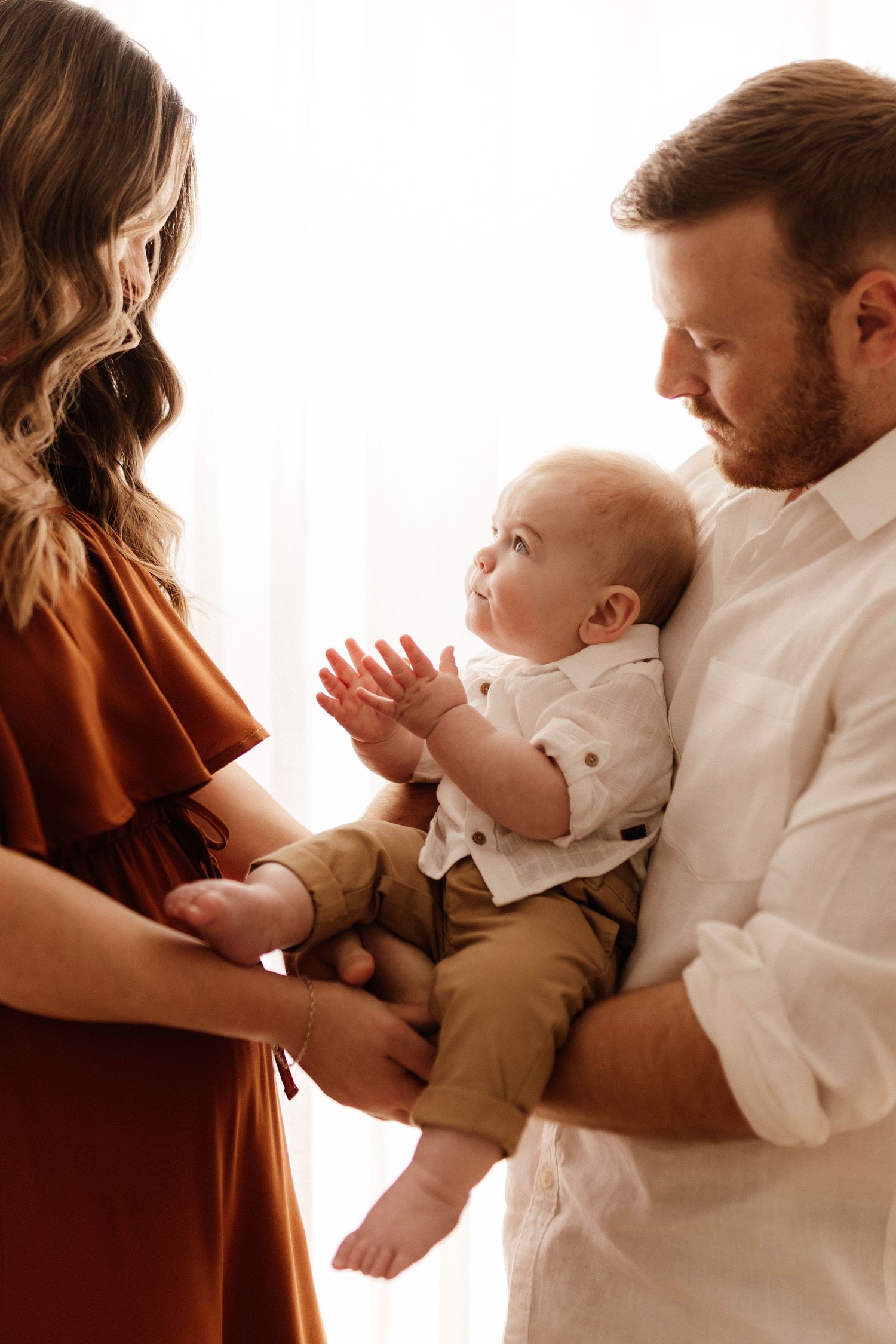 Intimate family moment captured in soft window light with baby in neutral tones.