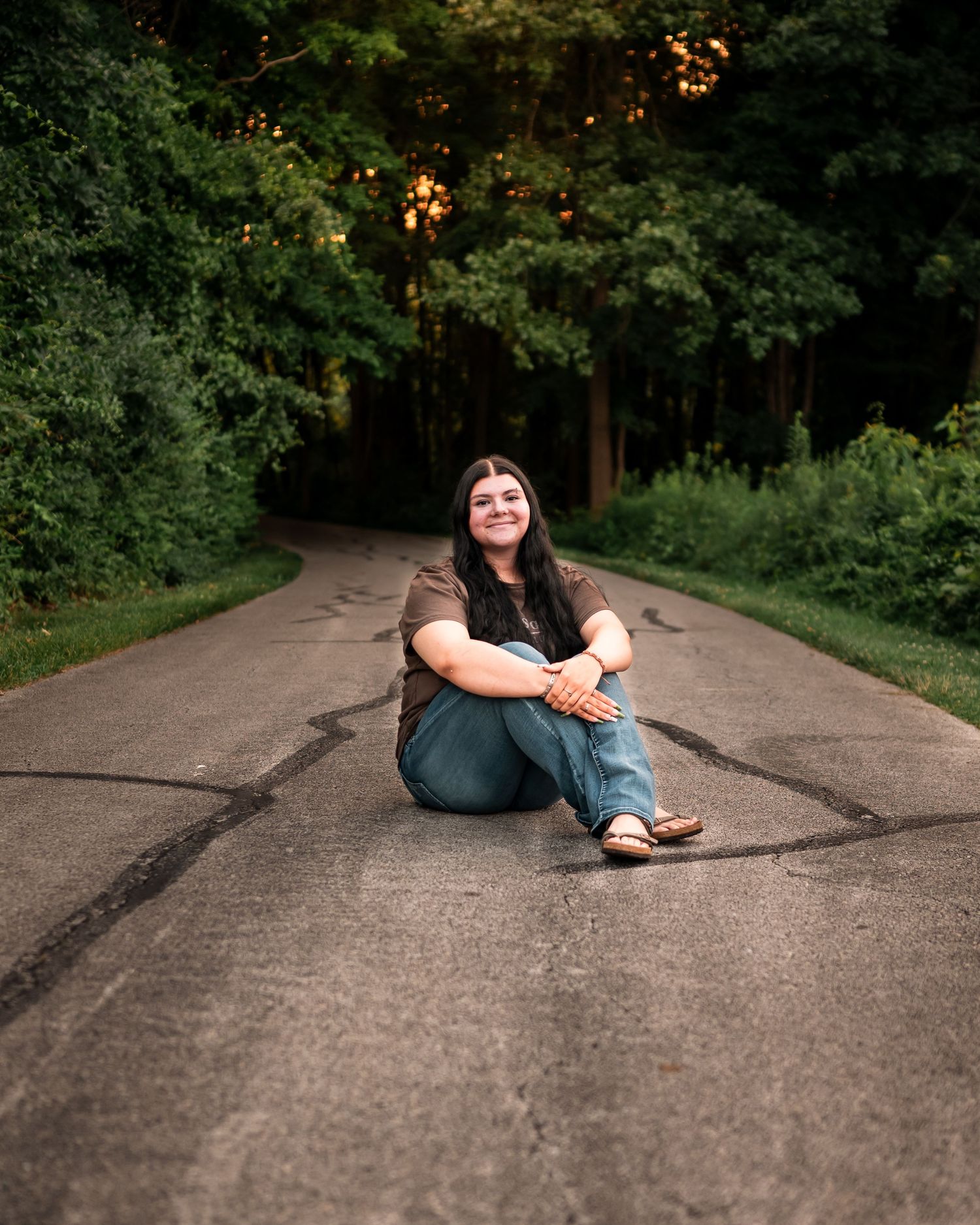 A person sits on a paved pathway surrounded by lush green trees in a series of artistic poses.