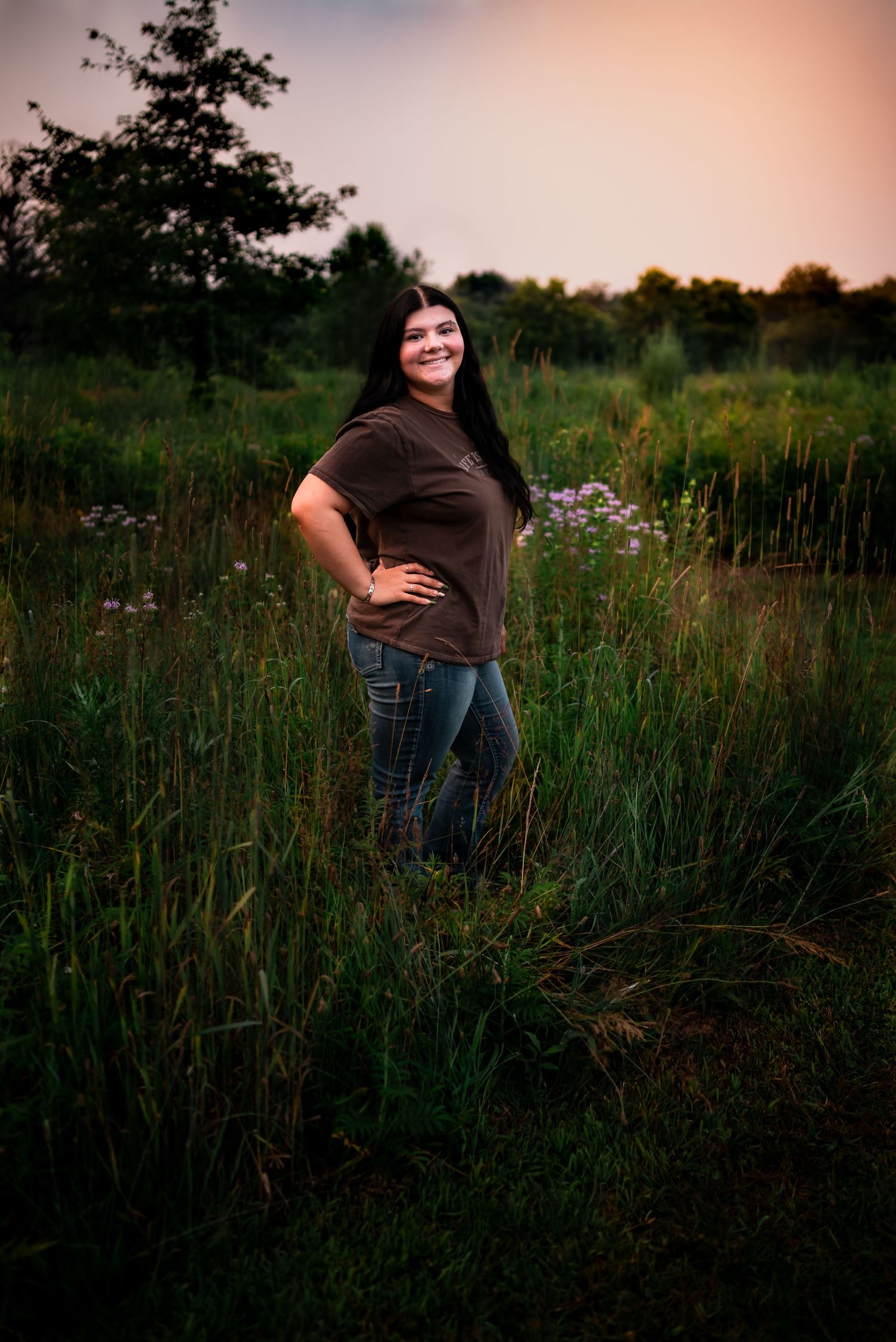 A maternity photo session in a wildflower meadow at sunset with tall grass and soft lighting.