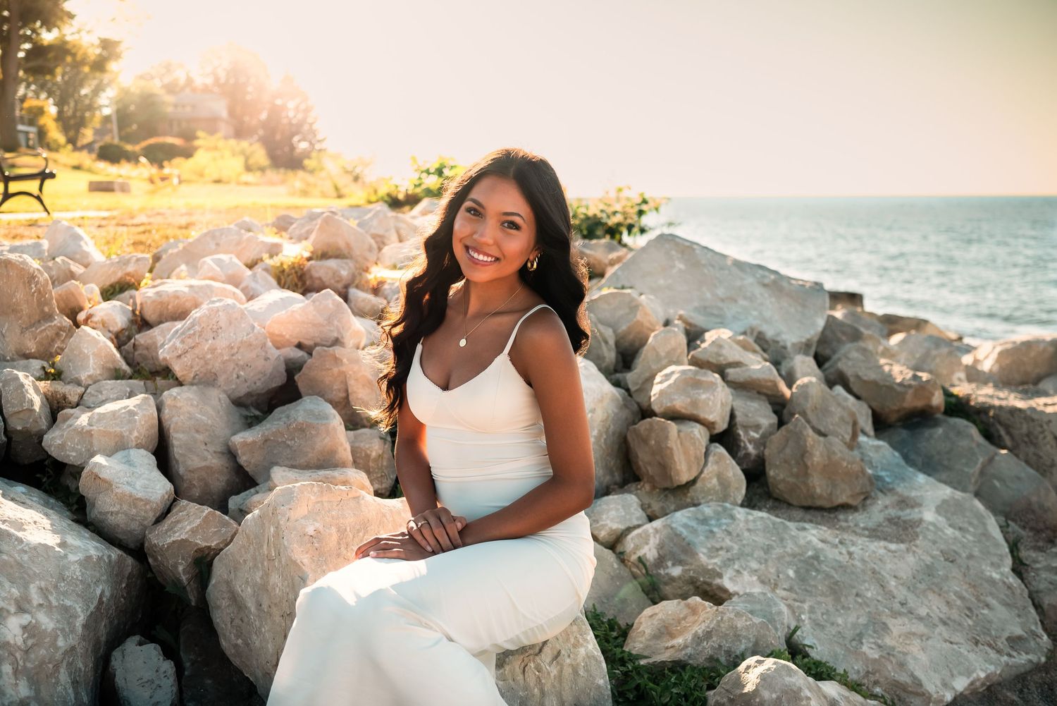 A beachside photoshoot at sunset with a white dress against rocky coastal backdrop.