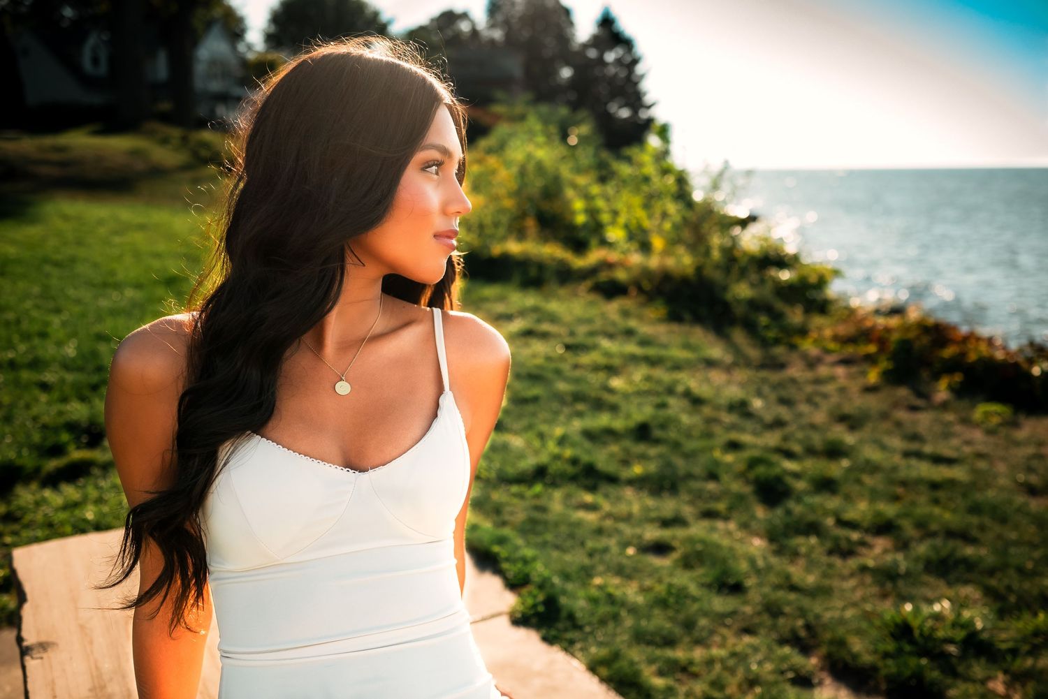 Person in white tank top smiling while enjoying a sunny day outdoors near the coast.