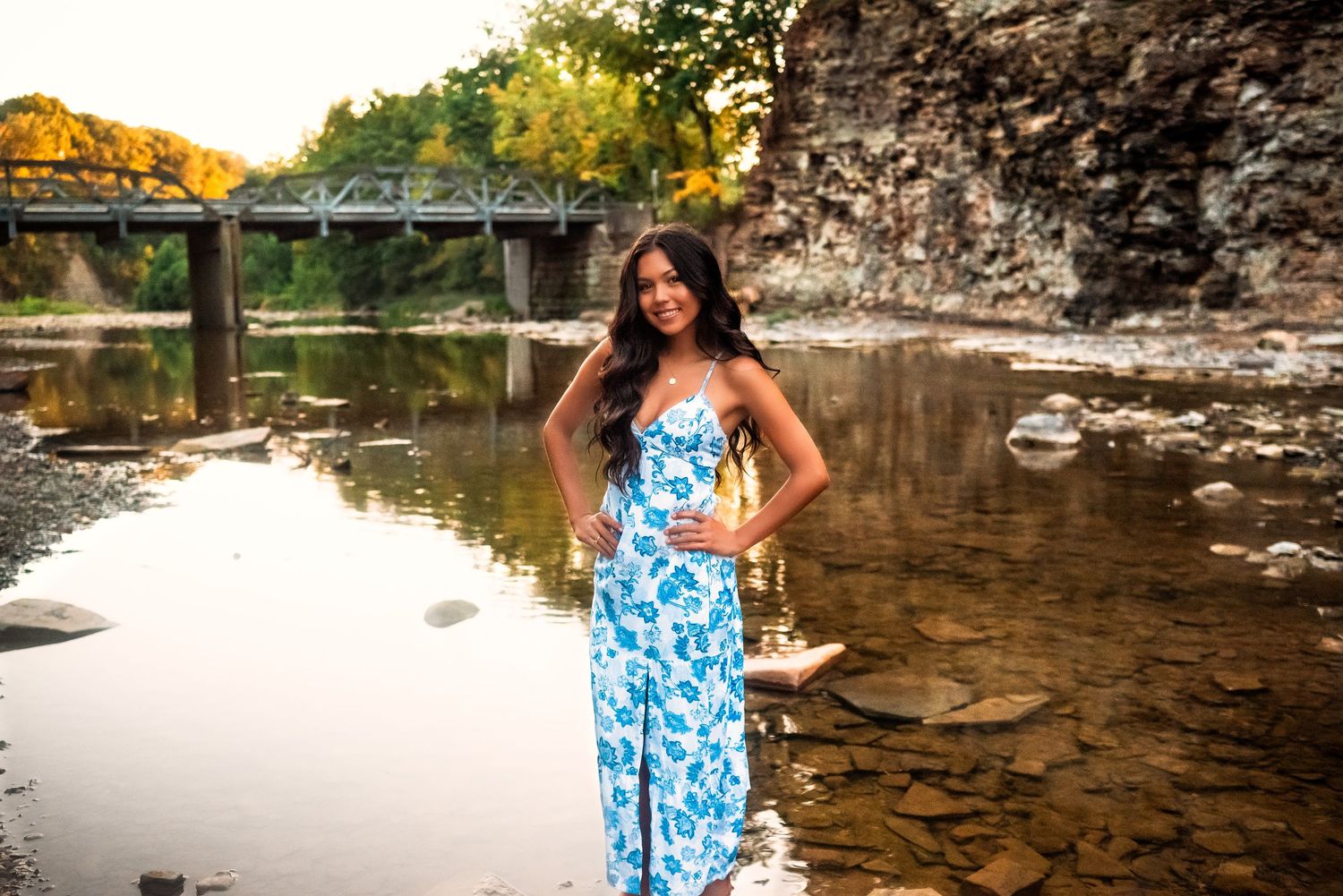 A scenic photoshoot at a rocky creek with flowing water and golden sunlight filtering through autumn trees.
