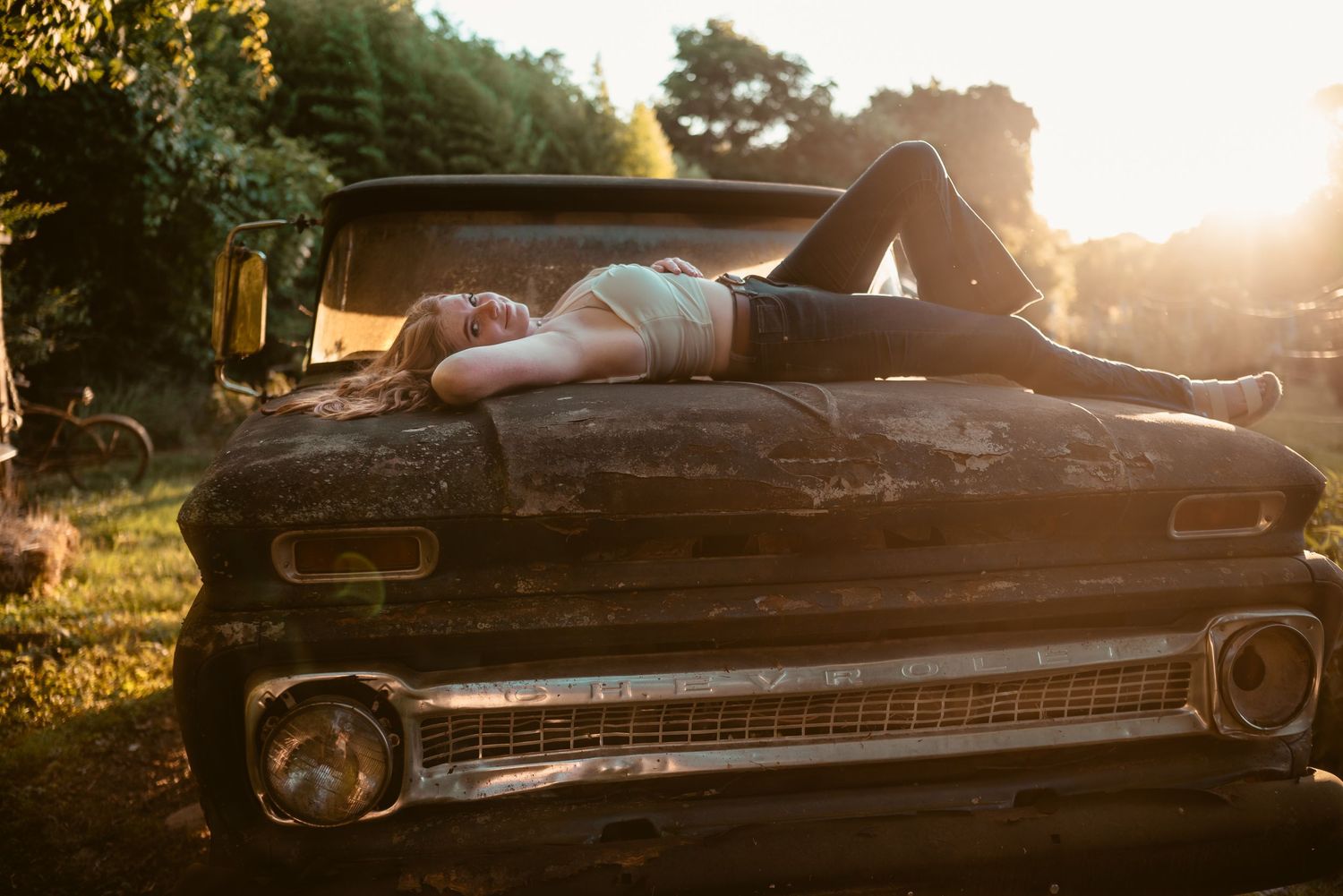 Vintage car silhouetted against golden sunset in rural setting.