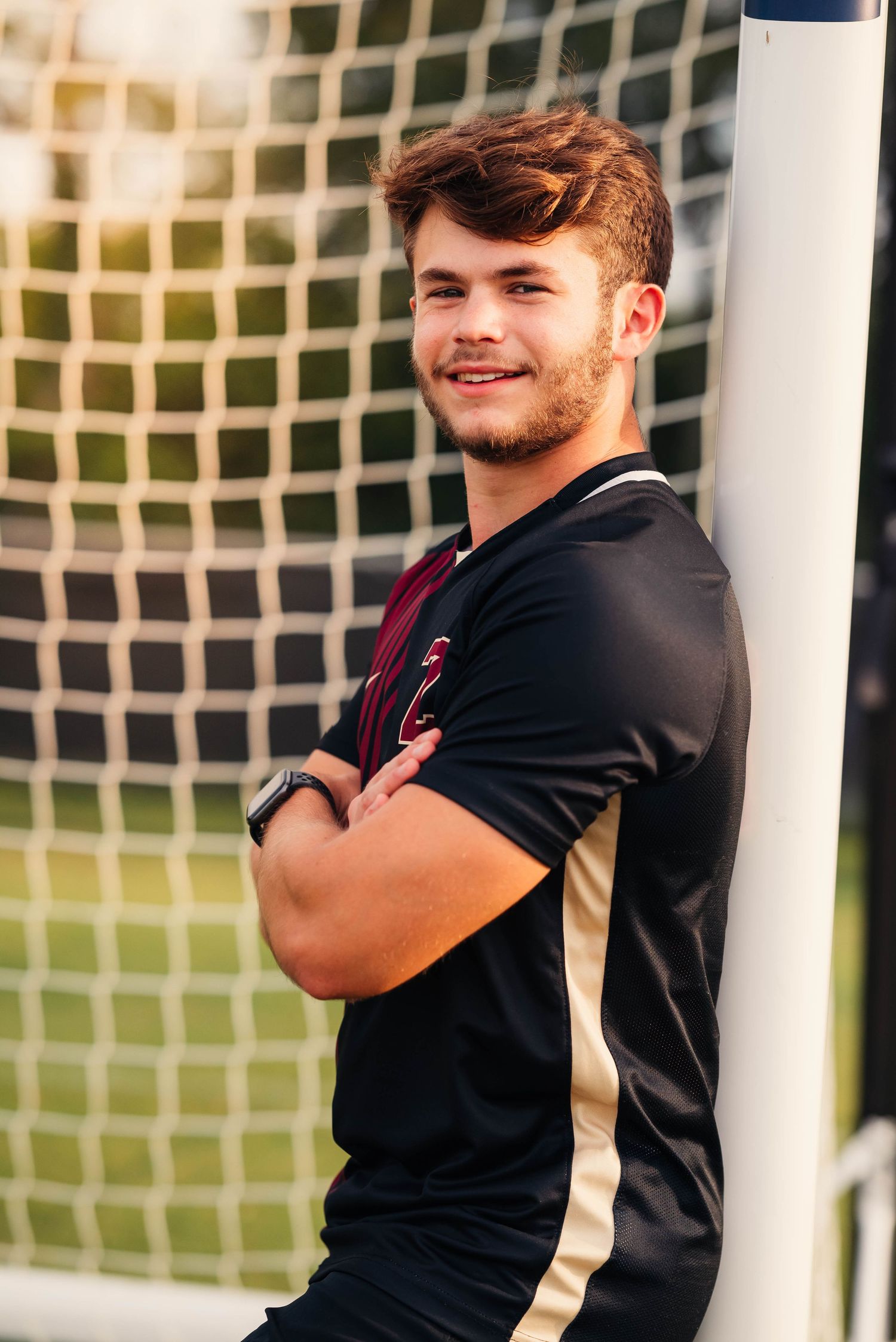 Athletic figure in black workout attire smiling against a soccer goal background.