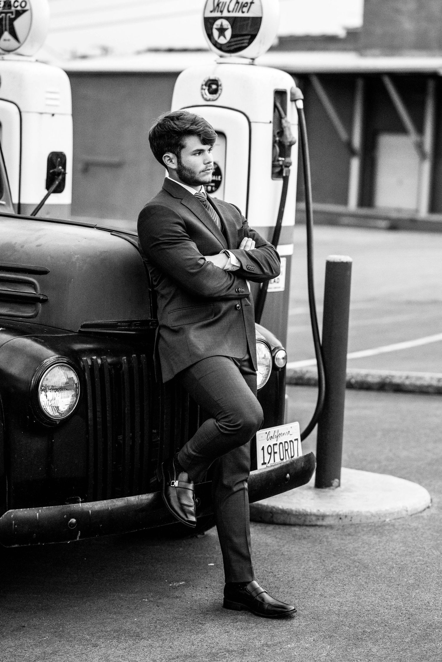 Black and white photos showing person in suit posing near vintage car.