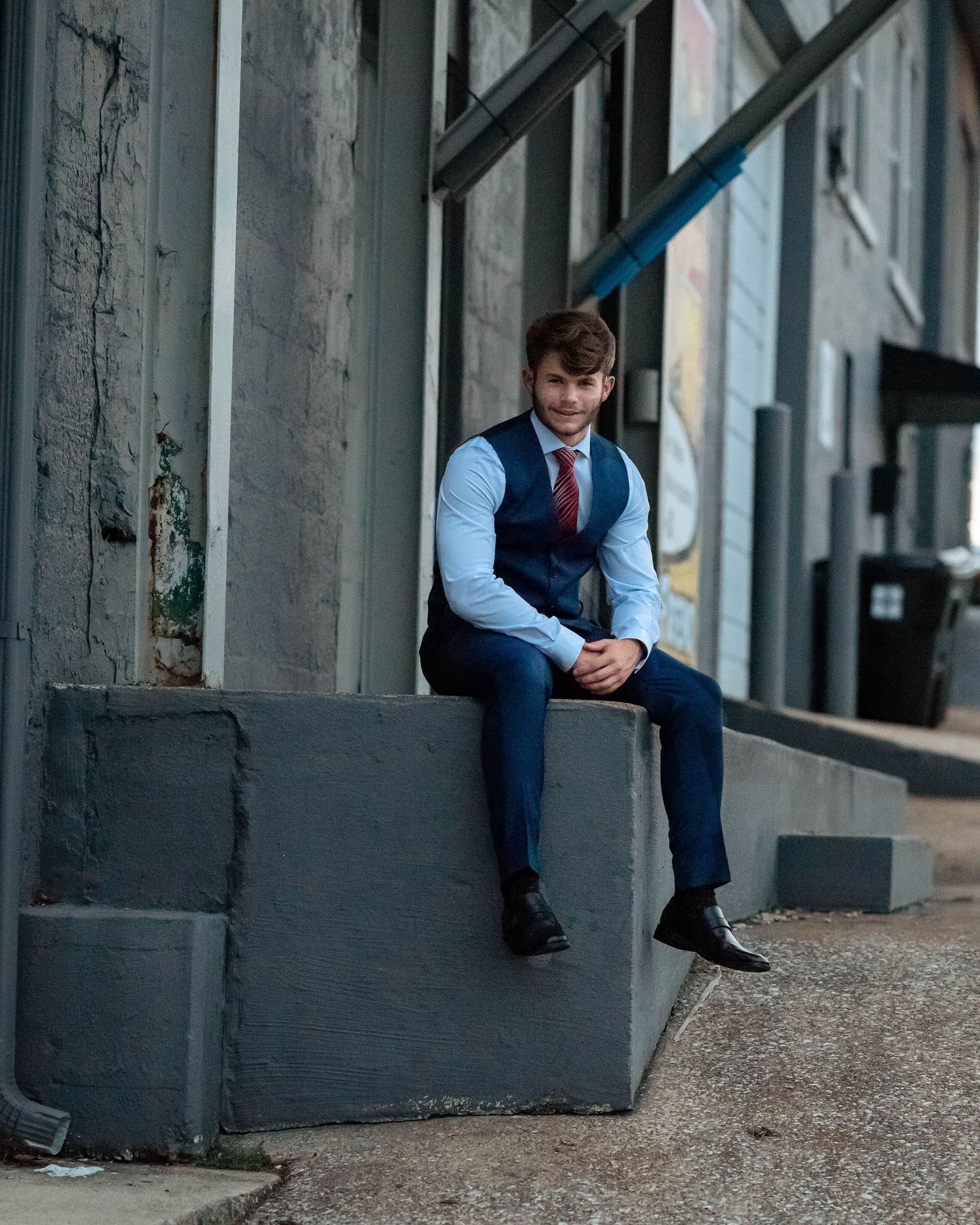 Professional portraits in blue suit and tie against industrial backdrop.