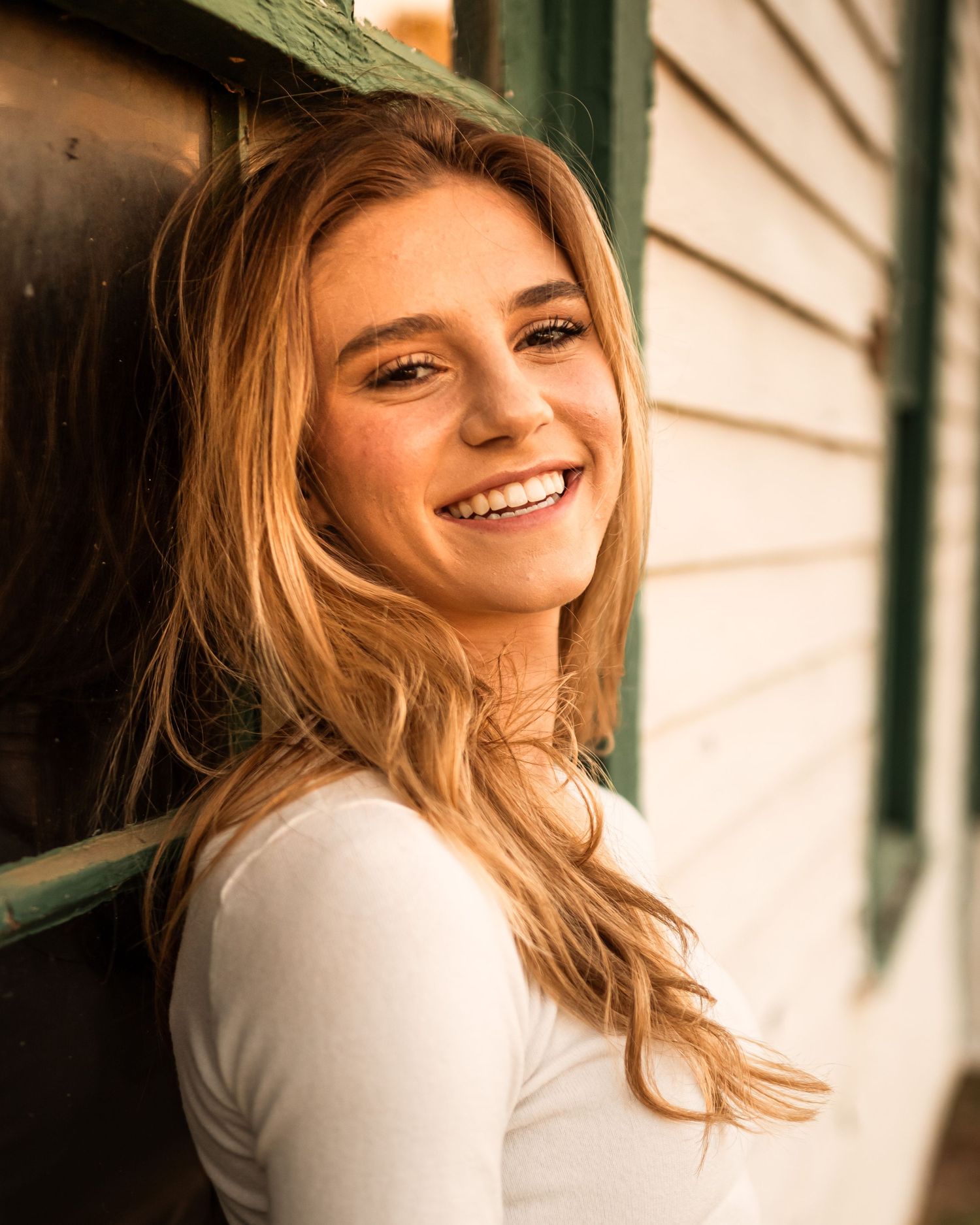 A warm-toned portrait against white siding with natural lighting.