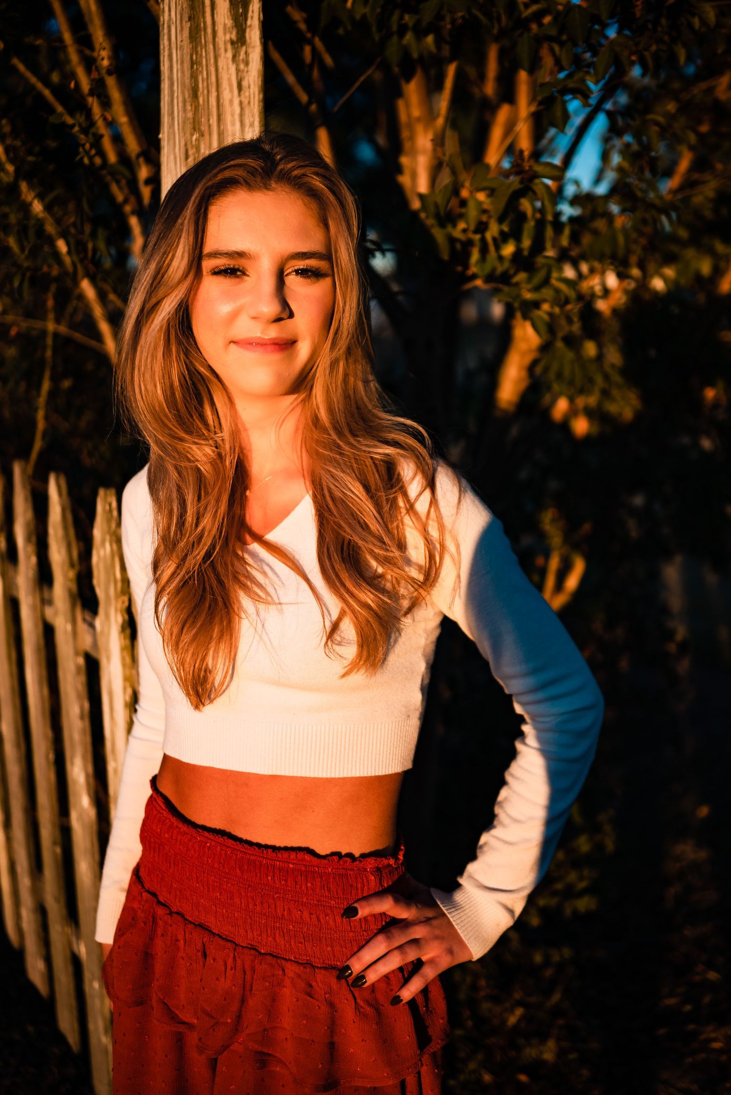 Golden hour portrait session with white fence and trees in background.