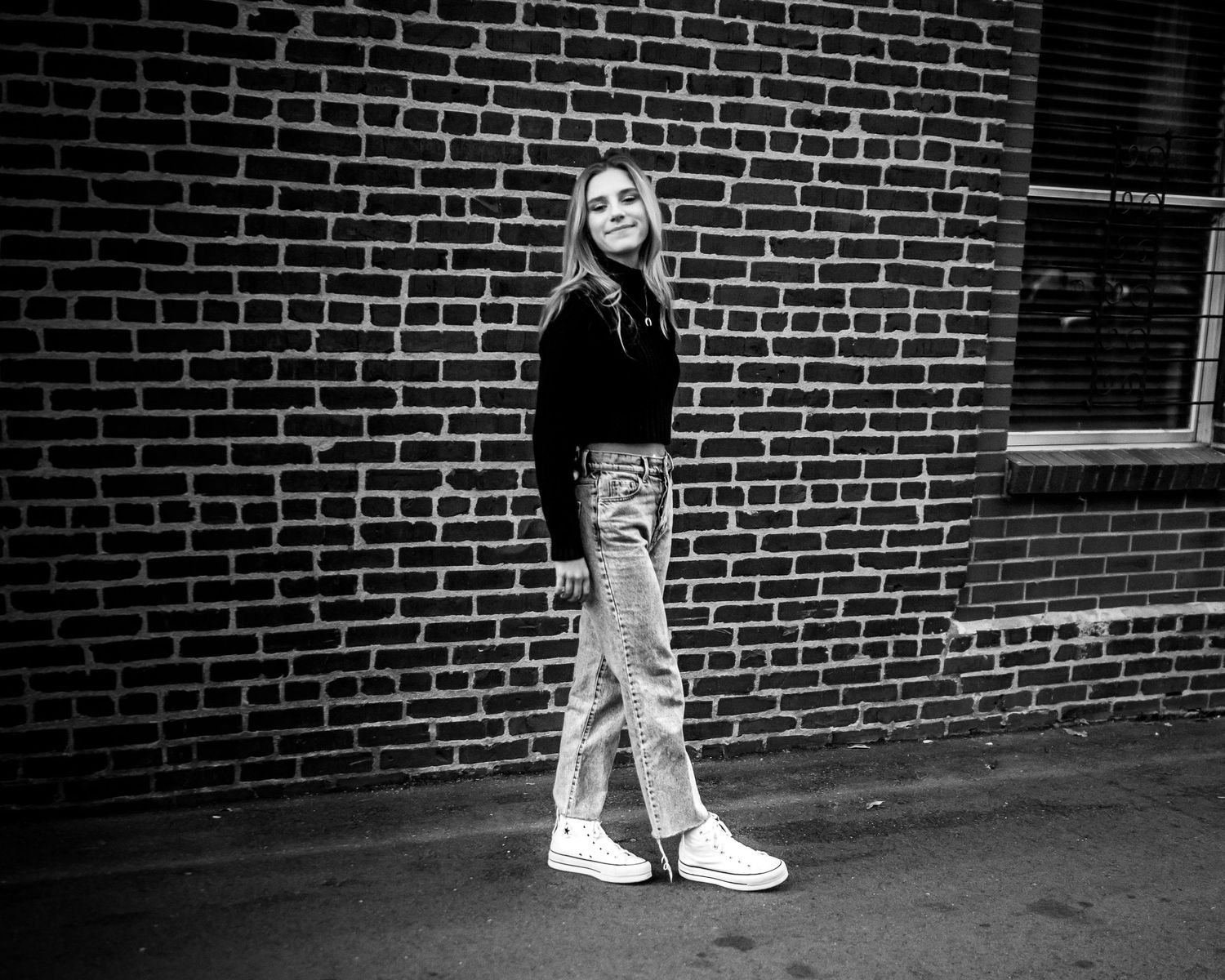 Close-up of white sneakers against a brick wall in an urban setting.