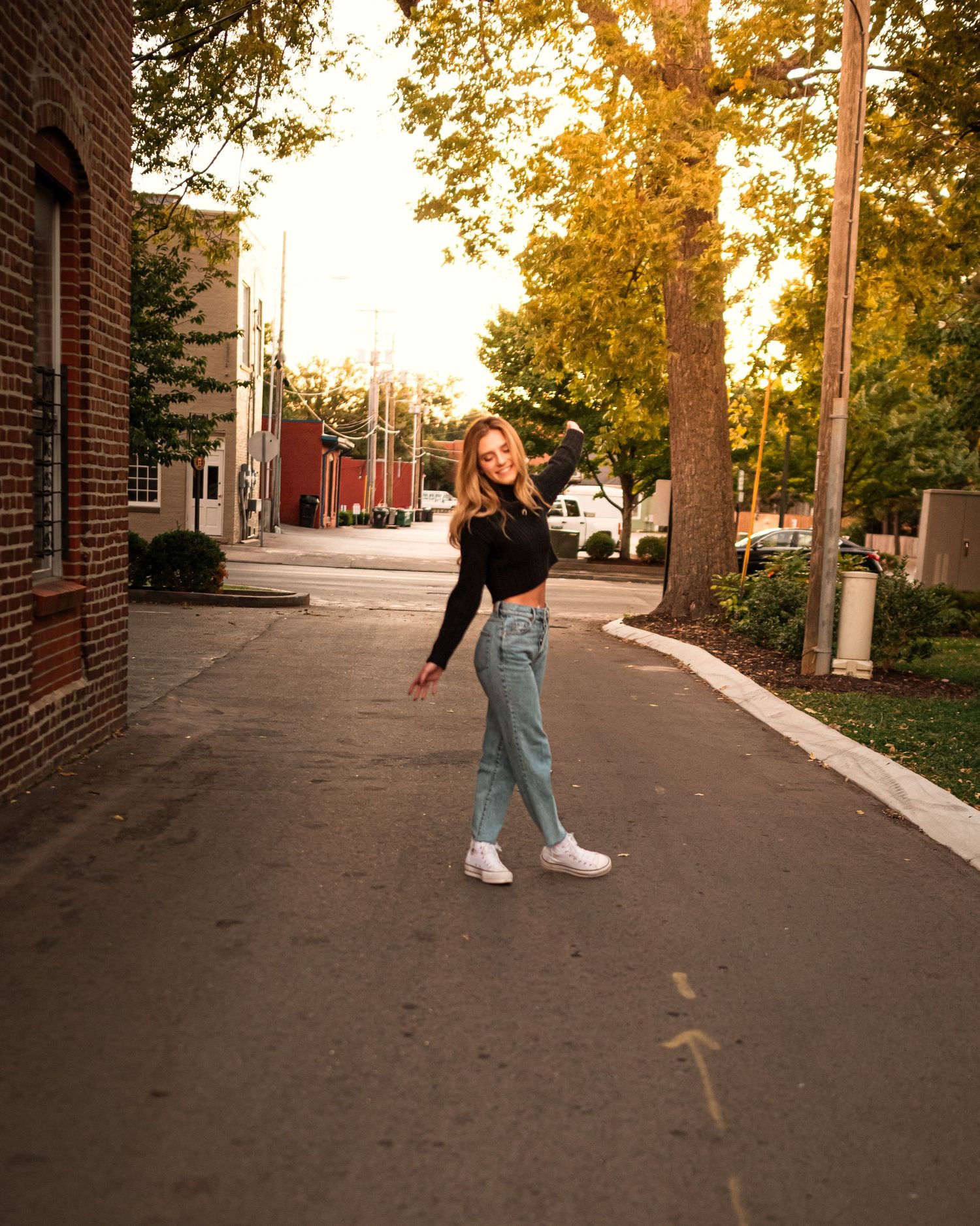Casual street fashion photography at sunset with brick wall and trees in background.