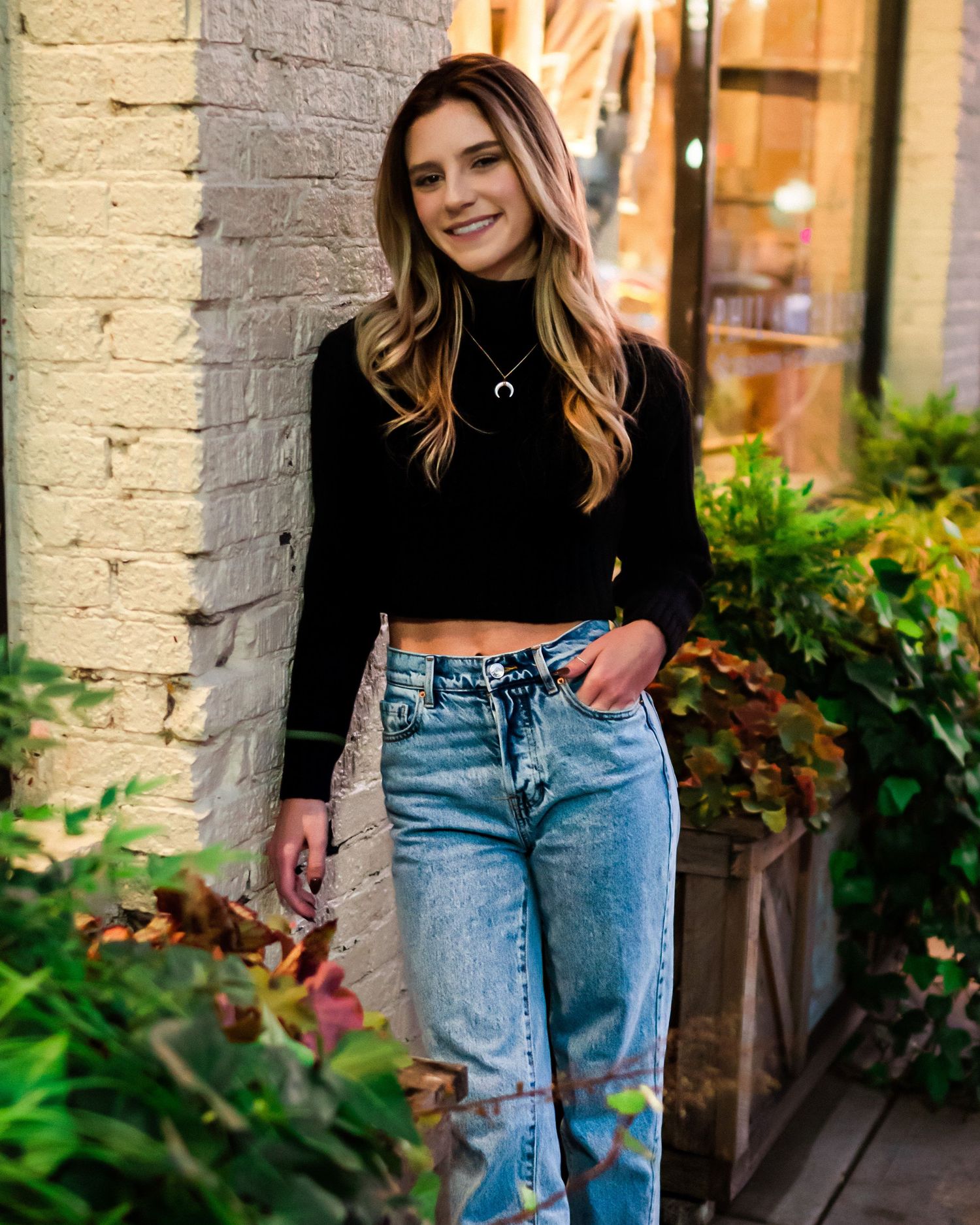 Fashion photography against textured brick wall with greenery and natural lighting.