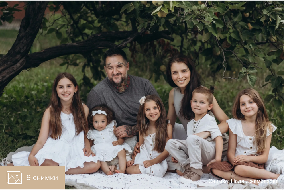 Family group photo taken outdoors with greenery and trees in background.